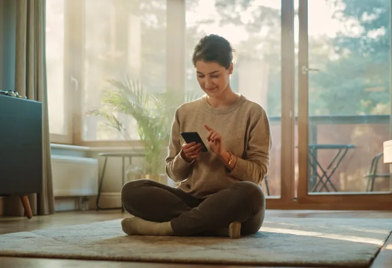 A woman in a sunlit room uses the Control4 smart home app on her phone